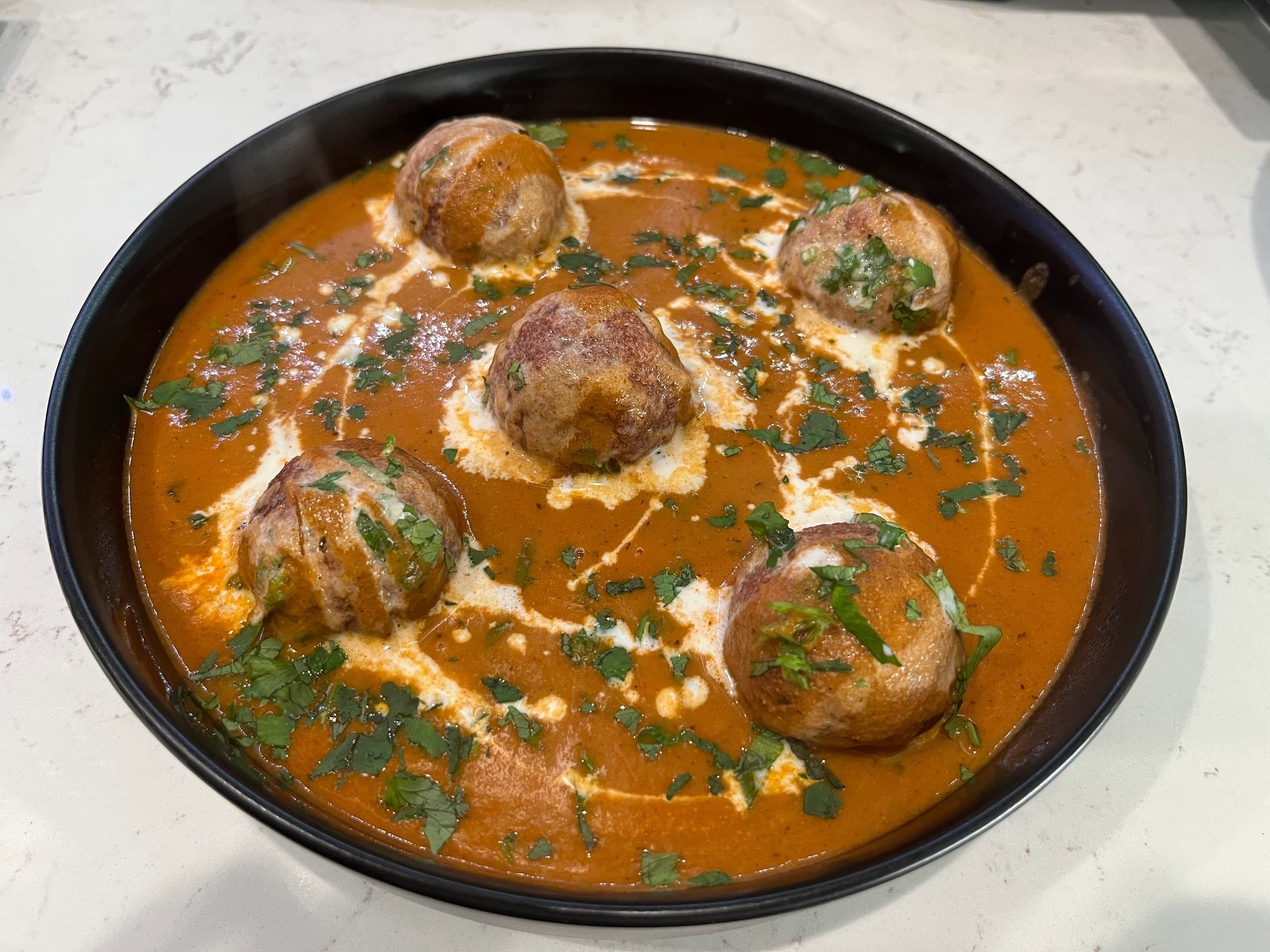 Malai kofta in creamy tomato gravy with cream swirls and cilantro