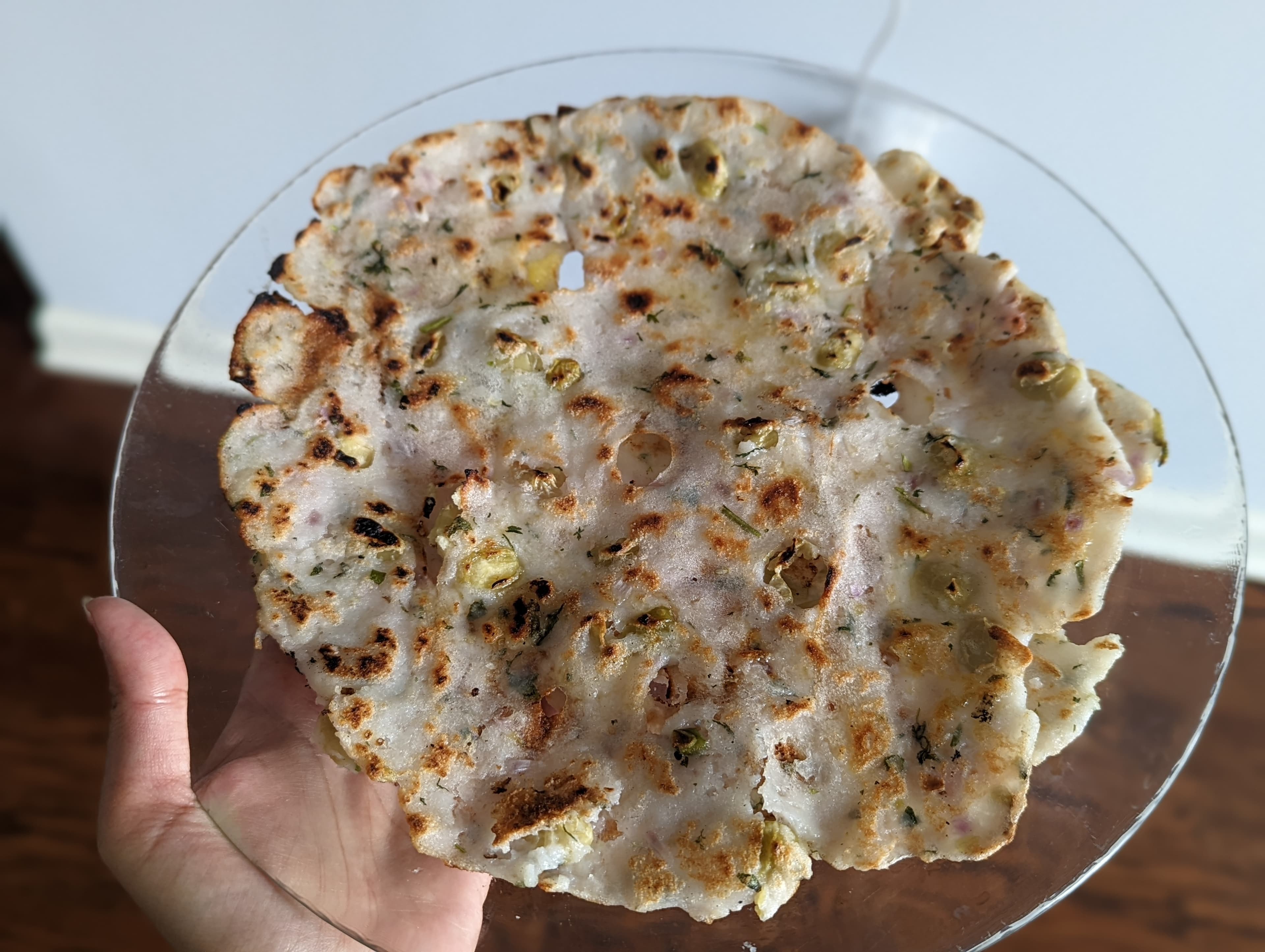 Akki rotti with onion and herbs on a glass plate, charred spots from the tawa